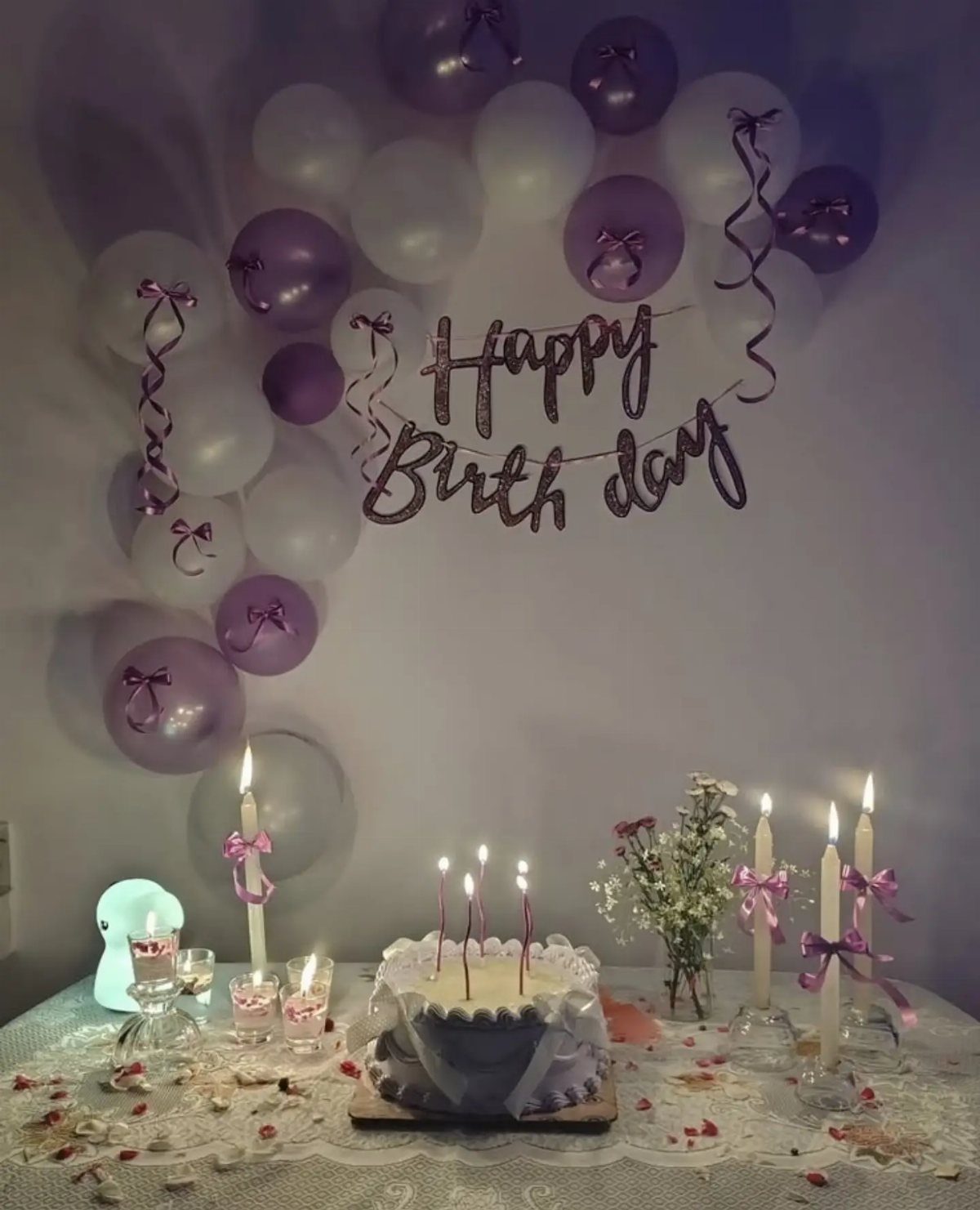 Birthday cake and candles on a lace table with purple balloon arch and banner.