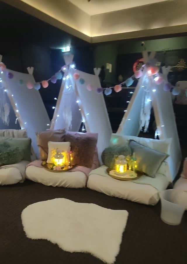 White teepee tents with fairy lights, colorful garlands, and plush cushions for a party.