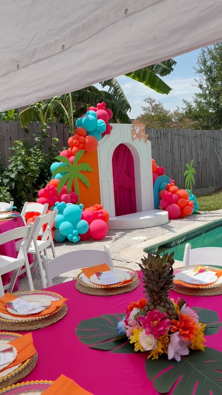 Tropical party setup with colorful balloons and a pink table next to a pool