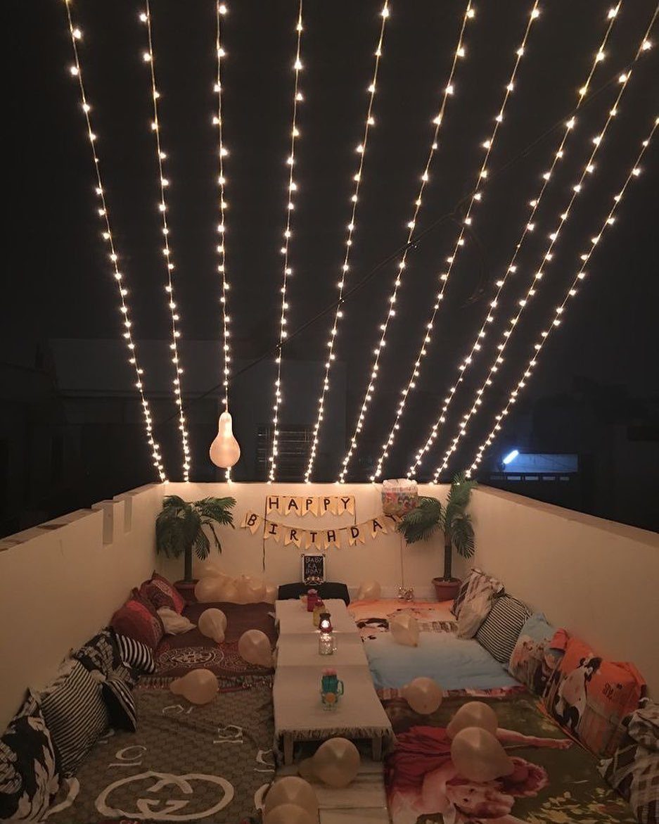 Rooftop birthday setup with overhead string lights, floor cushions, and birthday banner.