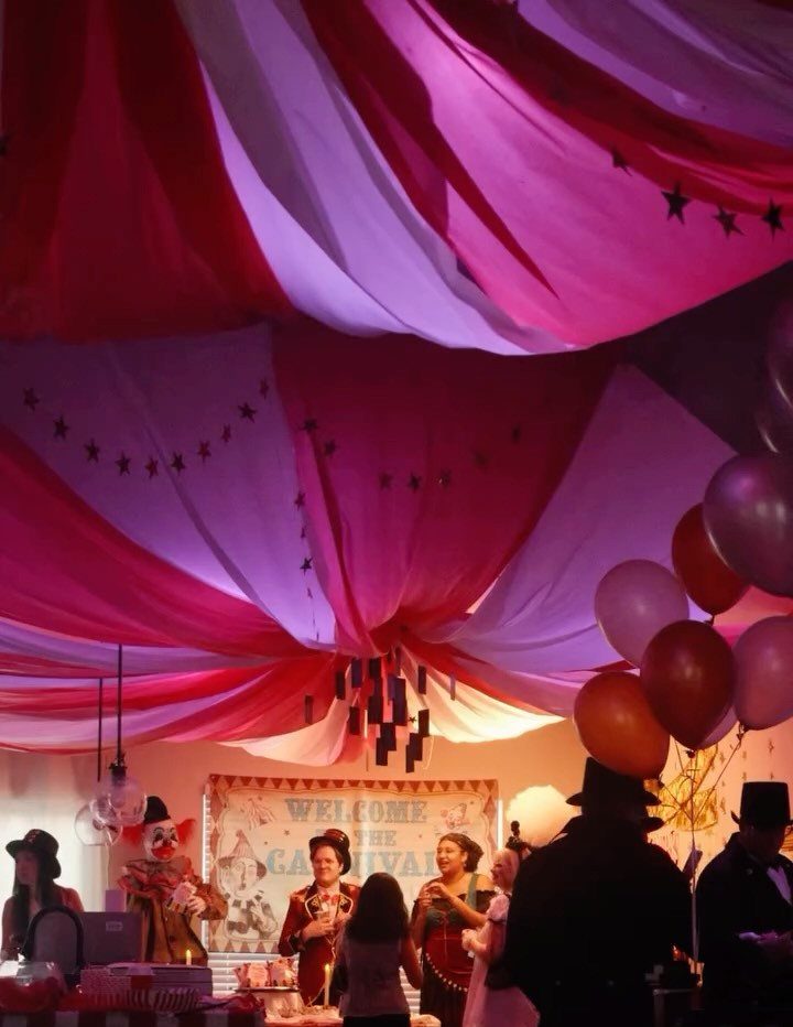 Costumed guests at a carnival themed party under red and white draped fabric.