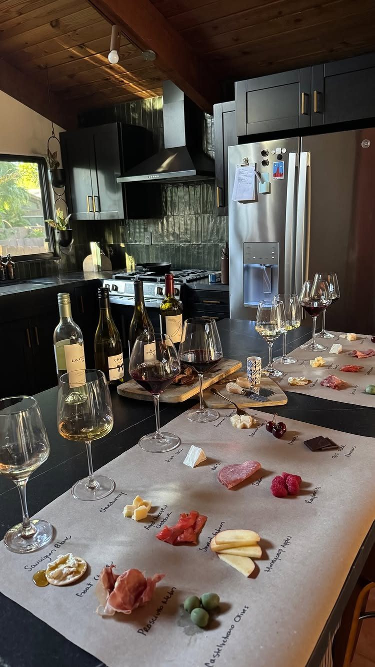 Wine tasting spread with glasses, bottles, and labeled appetizers on a kitchen counter.
