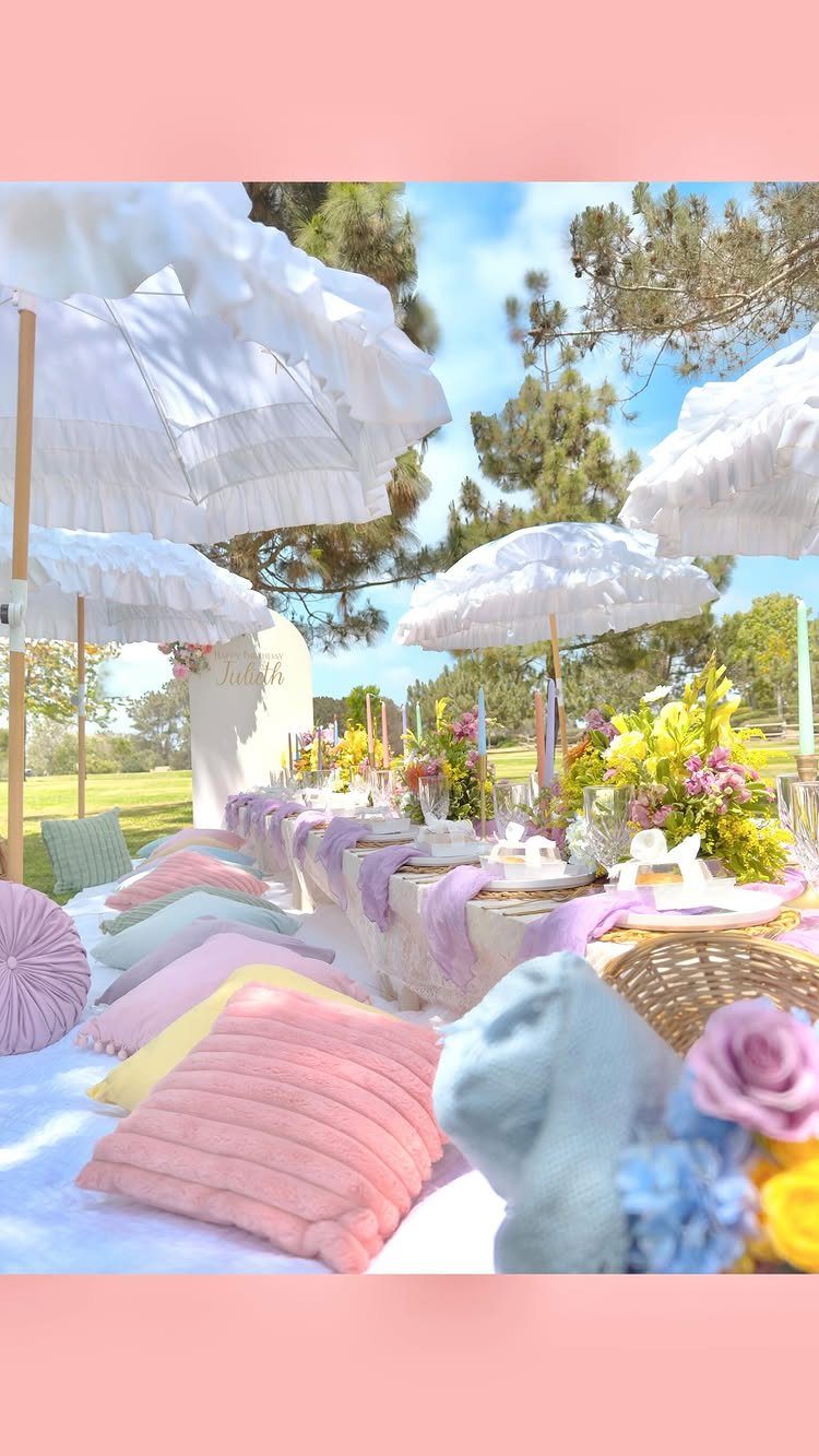 Lavish outdoor picnic setup with pastel pillows, flowers, and white lace umbrellas in park