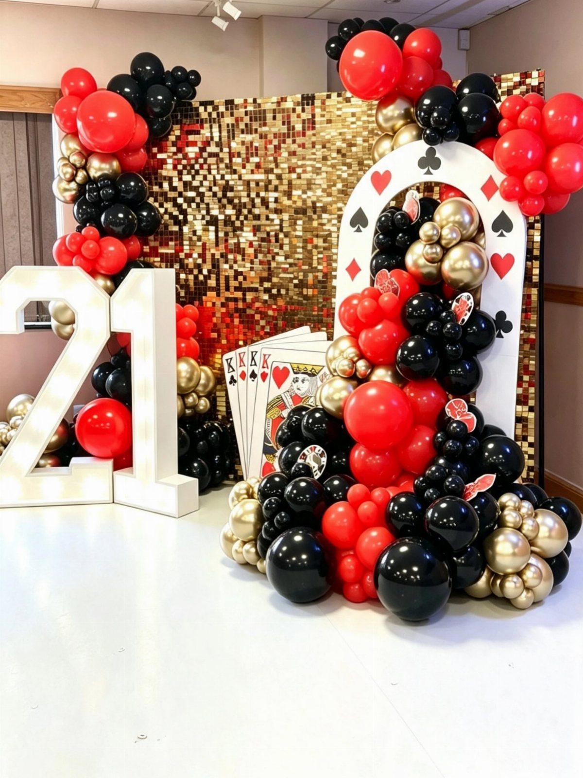 Red, black, and gold balloon arches with giant playing cards and number 21.