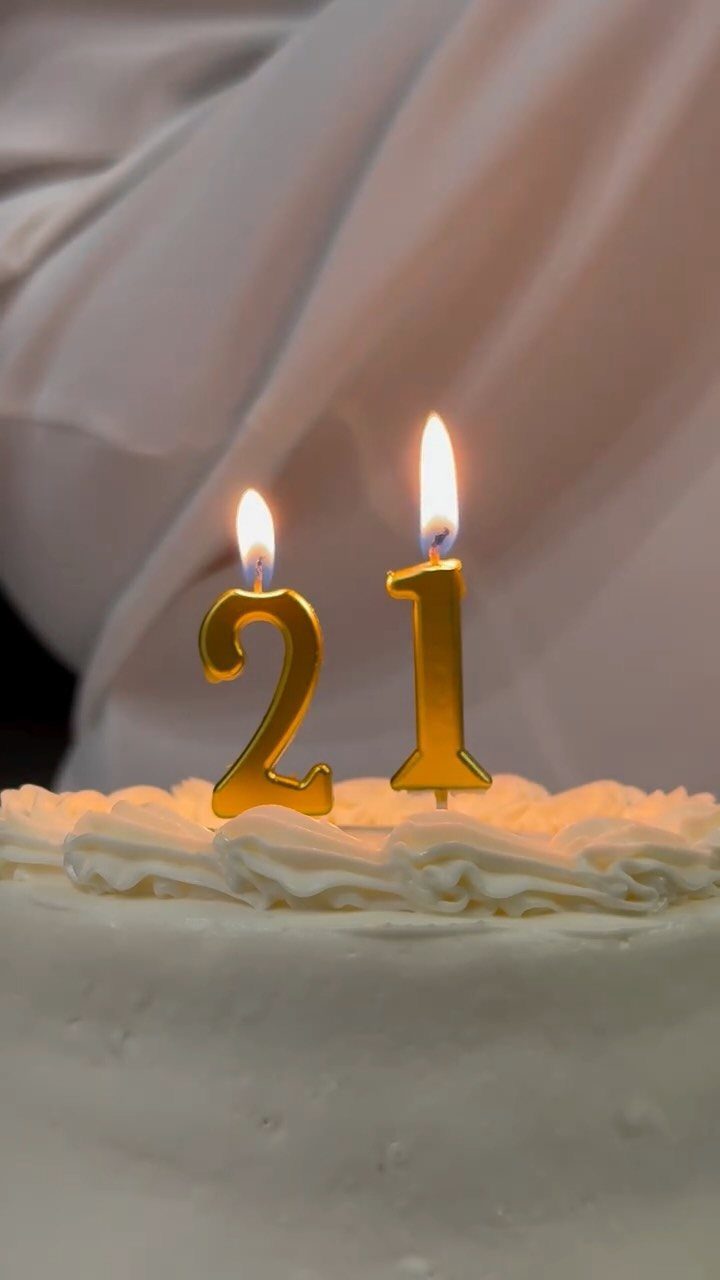 White frosted cake with lit gold number 21 candles against a white background
