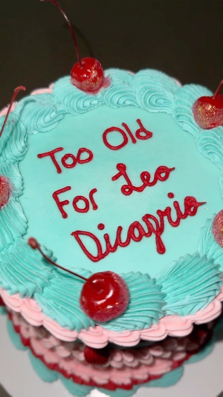 Blue and pink birthday cake with cherries and red text about Leo Dicaprio.