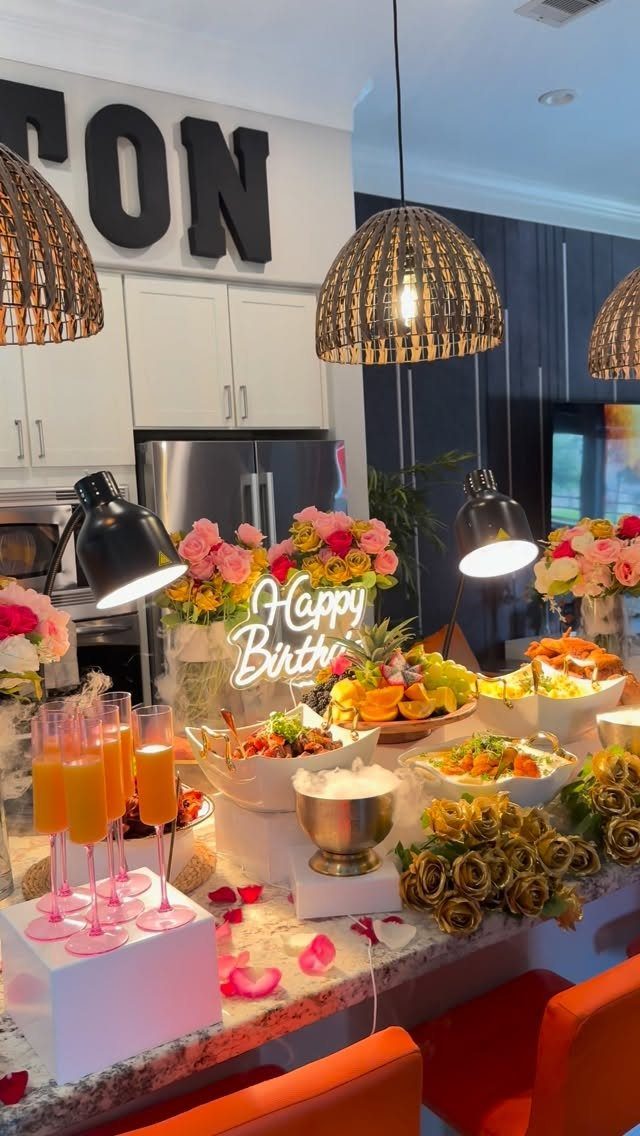 Birthday party food spread with neon sign, fruit platters, and orange cocktails.