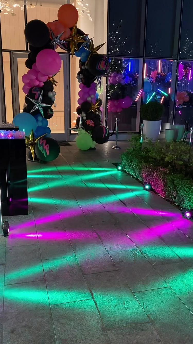 Colorful balloon arch and neon floor lights at a nighttime party entrance.