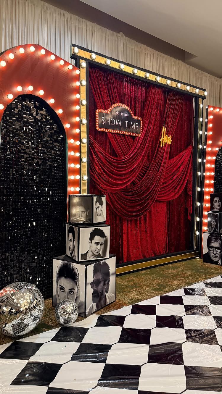 Theatrical photo backdrop with red curtains, marquee lights, and checkered flooring.