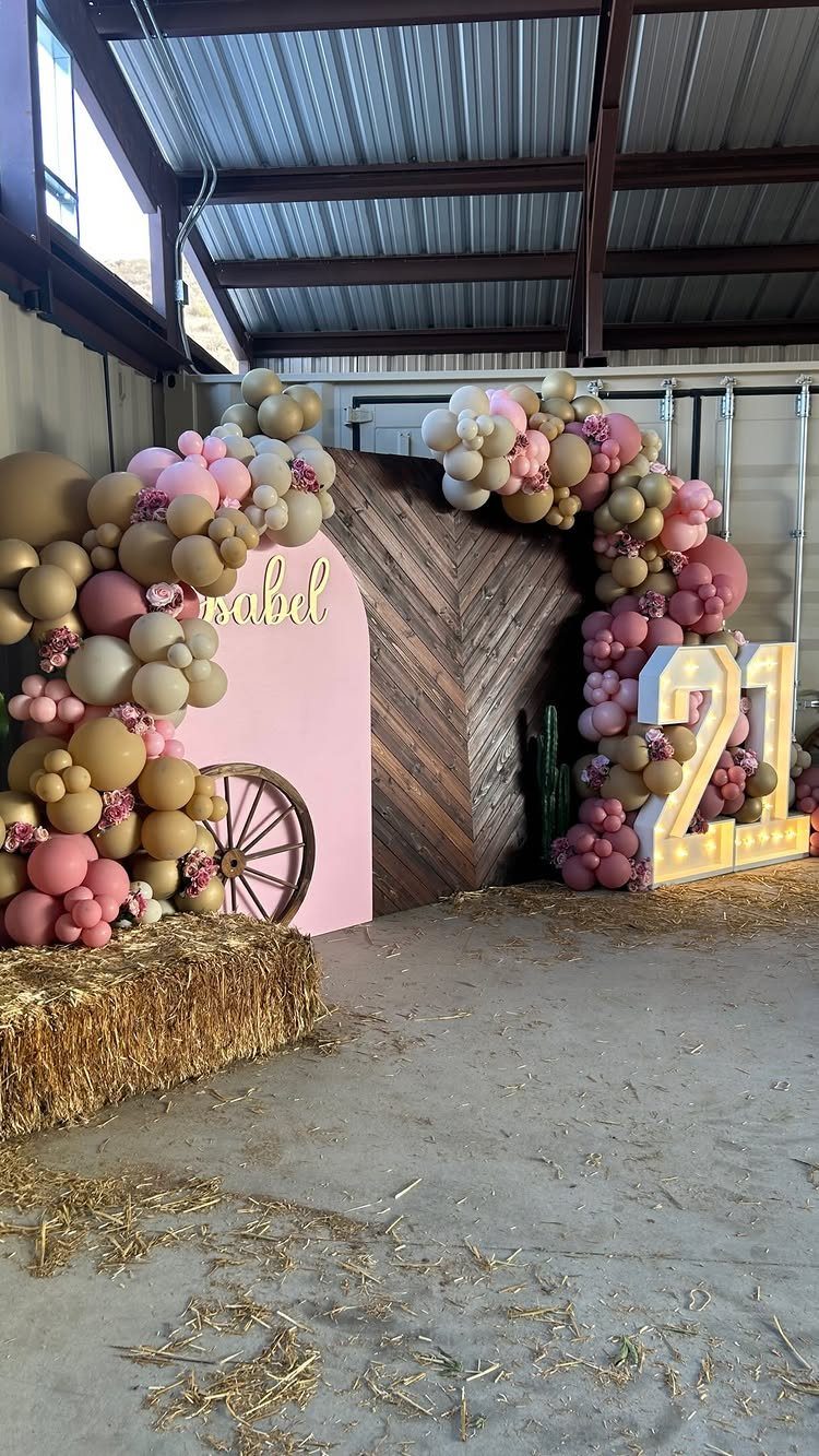 Party backdrop with pink and gold balloons, wooden barn door, and lit 21 numbers.