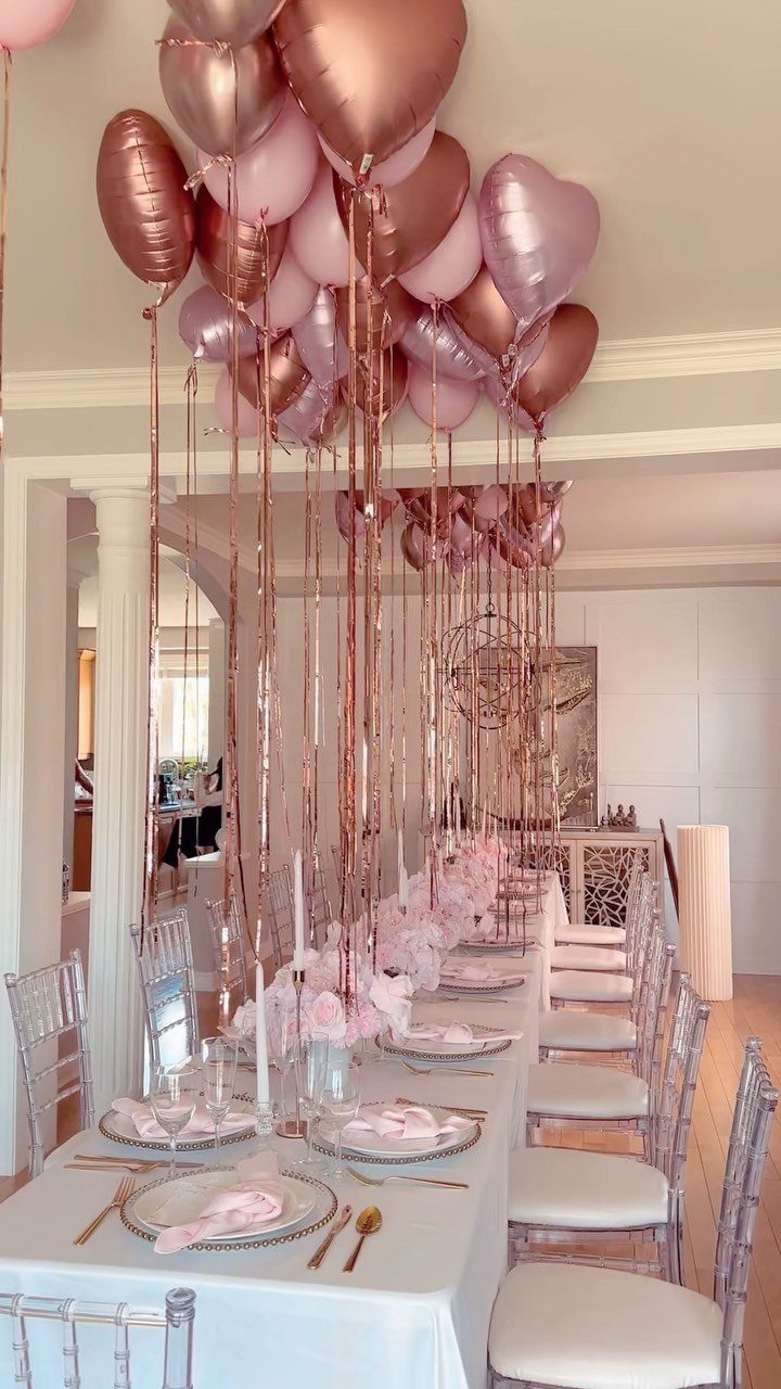 Dining table decorated with rose gold balloons and elegant place settings for a party.