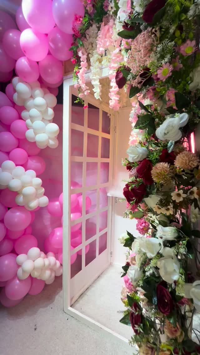 White door frame decorated with pink and white balloons and colorful floral arrangements.
