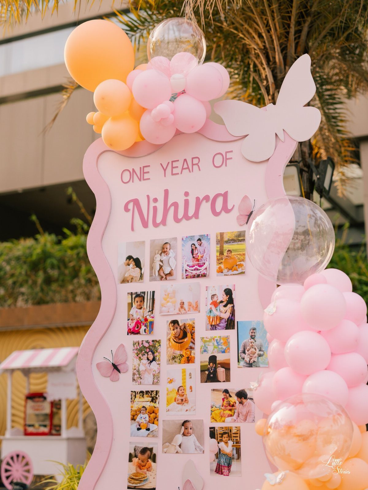 Pink decorative board with baby photos, balloons, and butterflies for a first birthday.