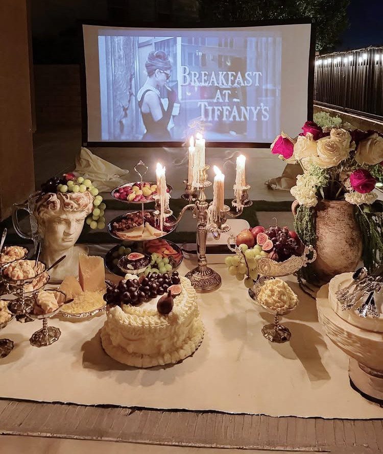 Outdoor movie screen showing Breakfast at Tiffany's behind a table of party food
