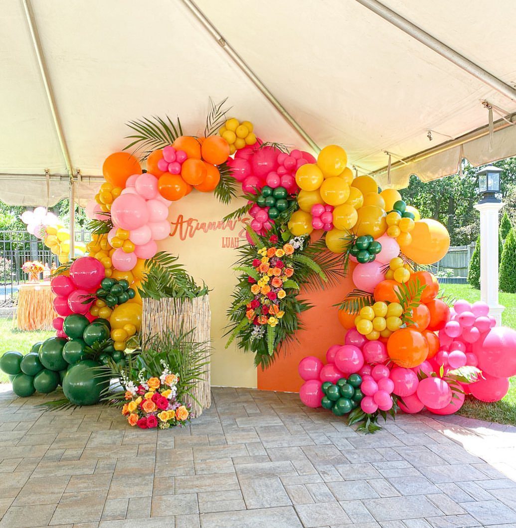 Tropical balloon arch with pink, orange, and yellow balloons and lush green foliage.