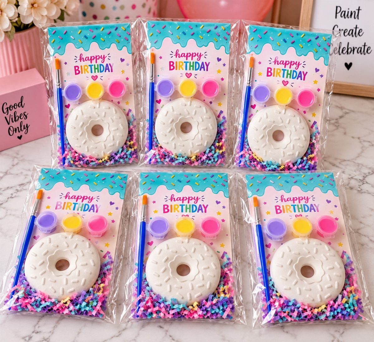 Six birthday party favor bags with white ceramic donuts and painting supplies.