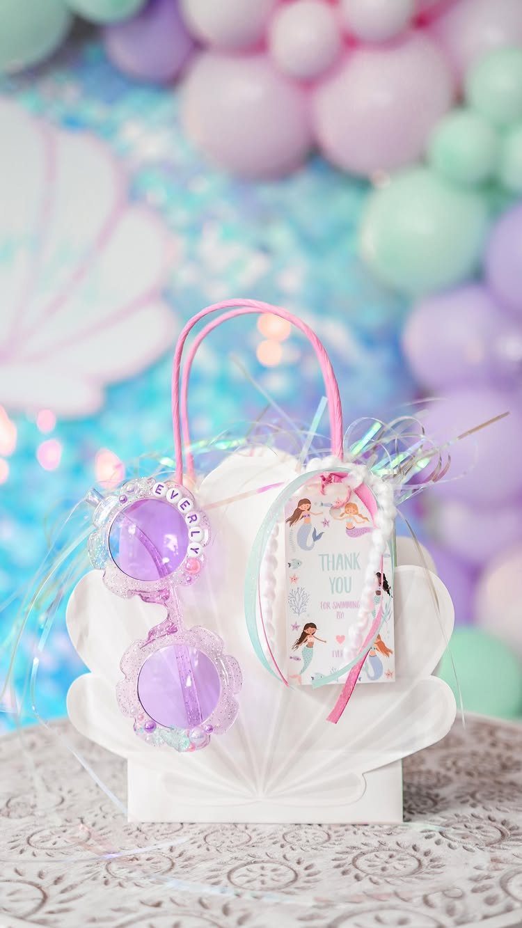 Shell-shaped white gift bag with purple sunglasses and a thank you card.