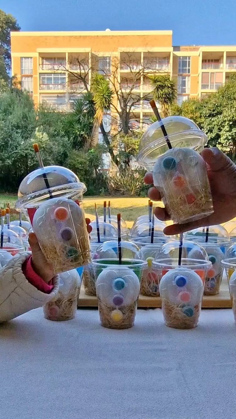 Clear plastic cups with dome lids filled with colorful candies and shredded paper.
