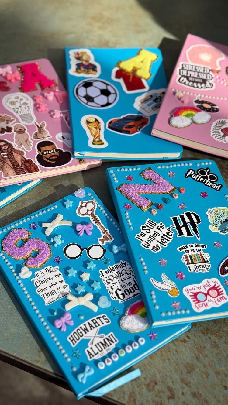 Decorated notebooks with colorful stickers, glittery letters, and charms on a table.