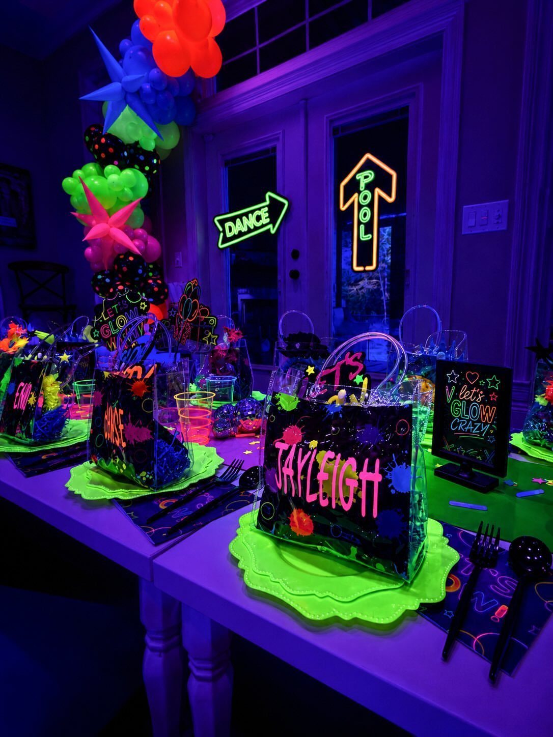Neon party table setup with glowing green plates and personalized black gift bags.