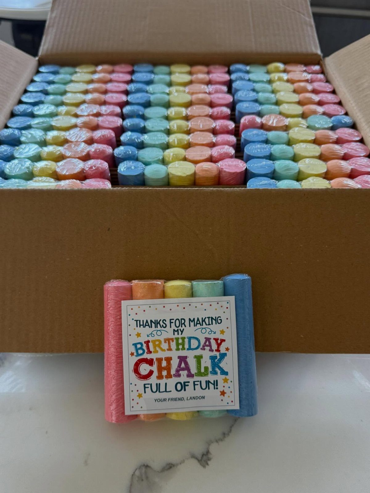 Colorful sidewalk chalk sticks in a box and a small bundled party favor.