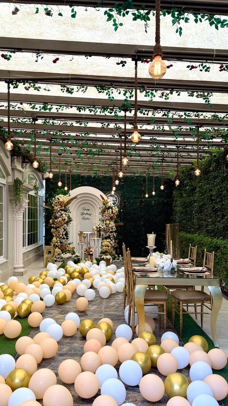 Covered porch party setup with balloons on the floor and hanging light bulbs.