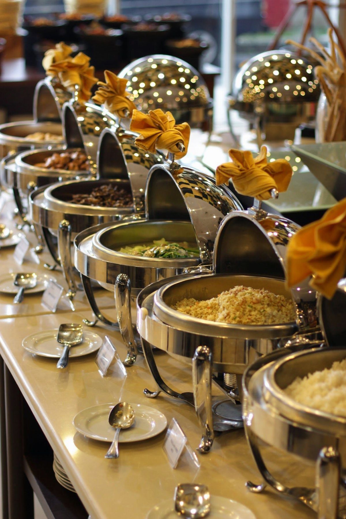 Silver chafing dishes with hot food arranged on a buffet table with napkins.
