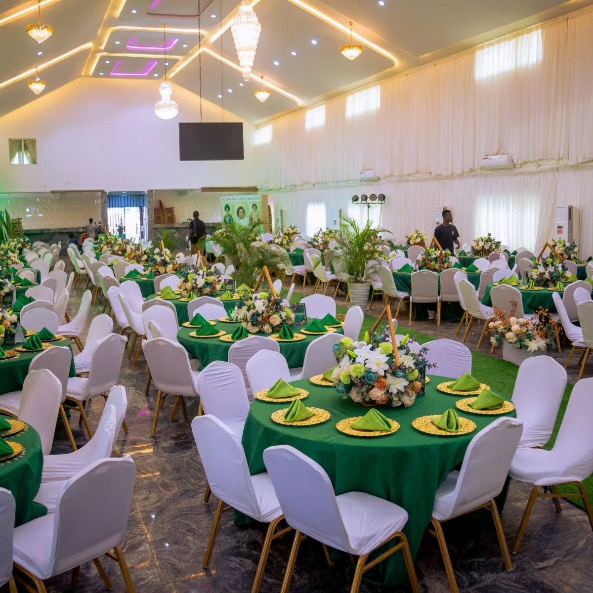 Event hall with round tables featuring green linens, white chairs, and floral centerpieces.