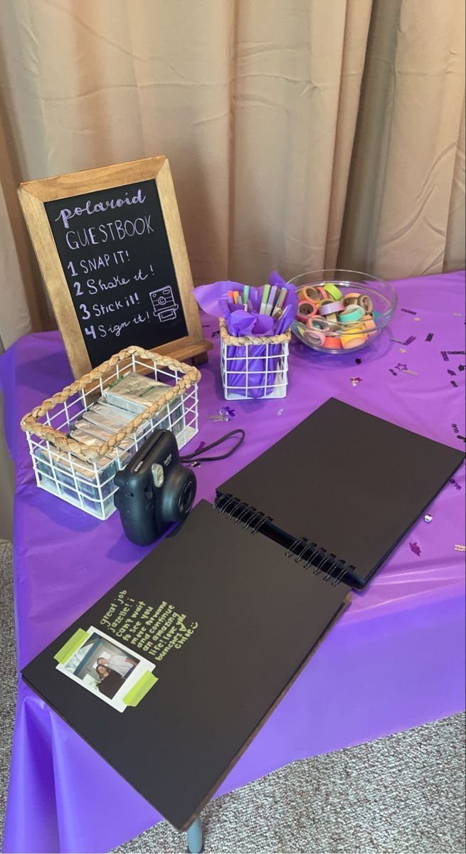 Polaroid guestbook station with camera, photos, and candies on a purple table.