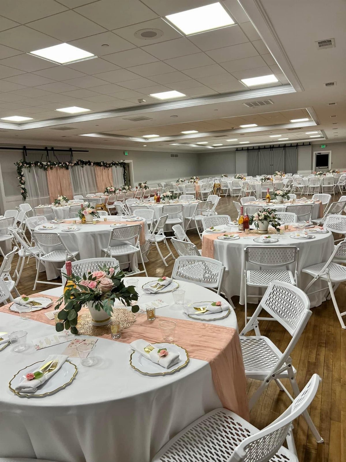 Banquet hall with round tables, white linens, peach runners, and floral centerpieces.