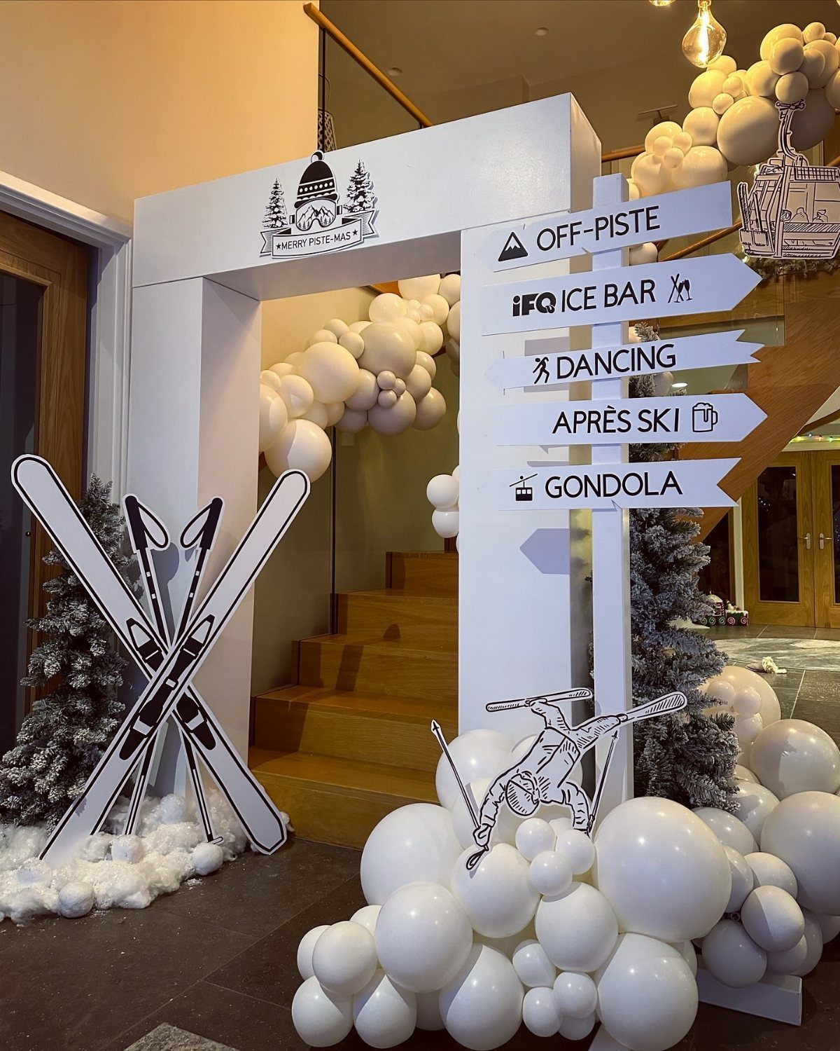 White event entrance with ski cutouts, a directional signpost, and white balloon clusters.