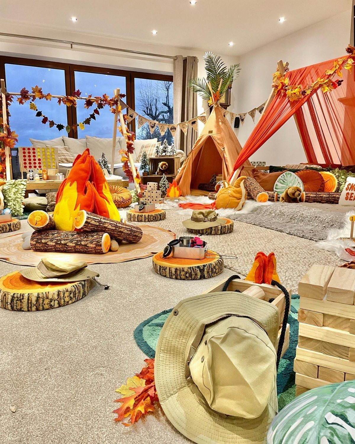 Indoor camping party setup with a teepee, faux campfire, and wood slice tables.