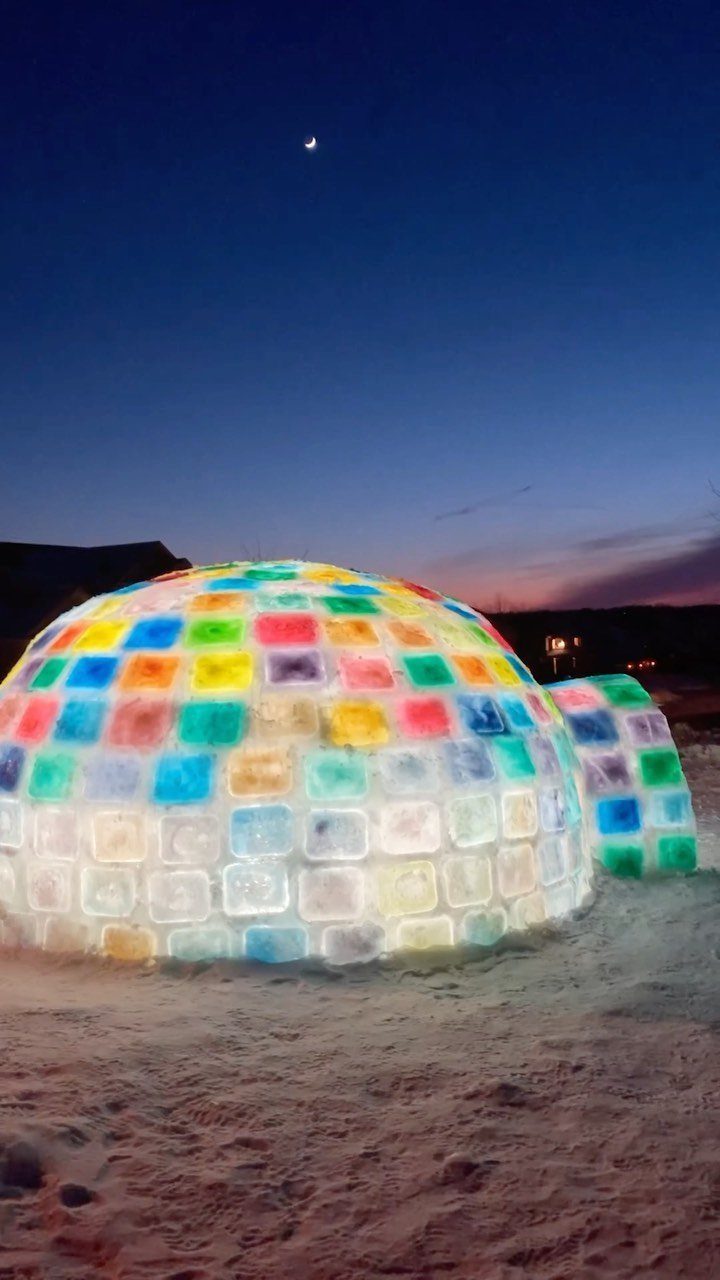 Glowing multicolored ice igloo dome on snow under a dark twilight sky