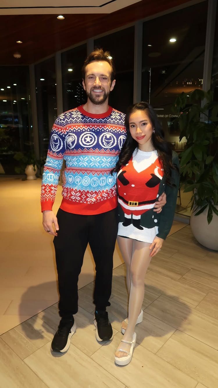 Man in a patterned winter sweater and woman in a Santa dress posing indoors.