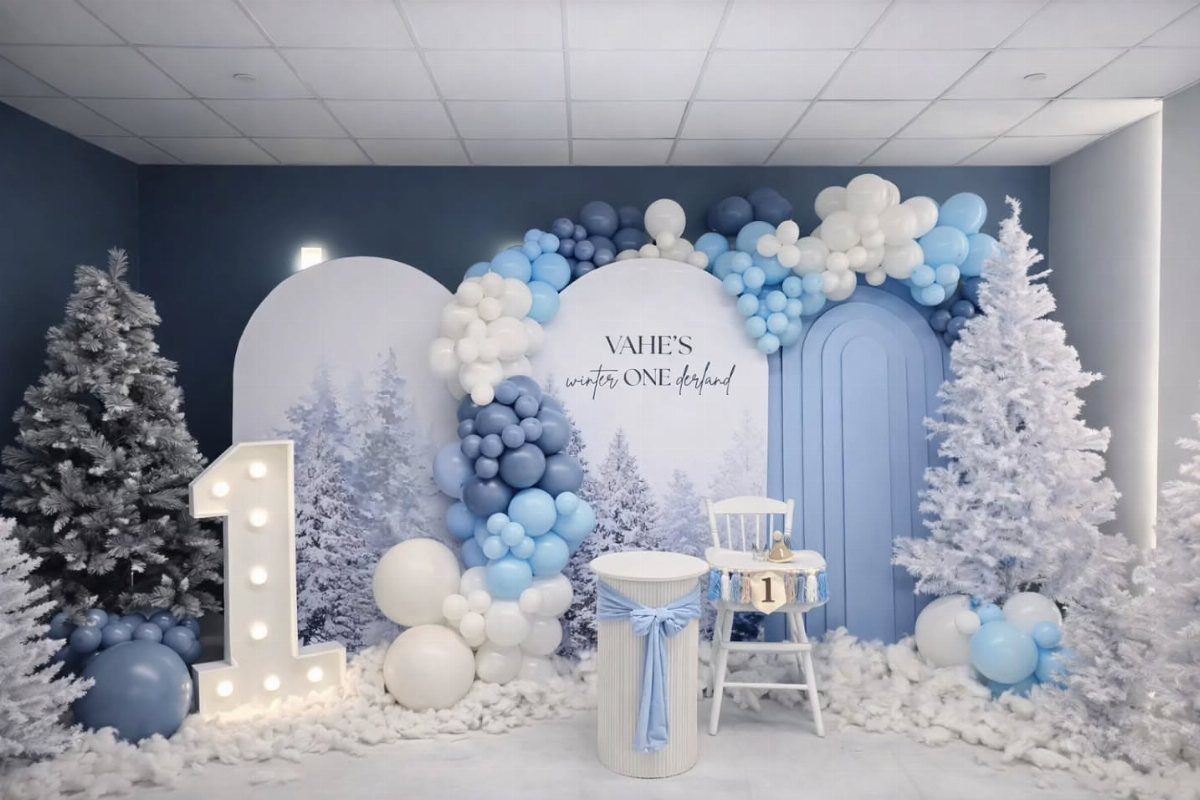 Winter themed first birthday party setup with blue balloons and white artificial trees