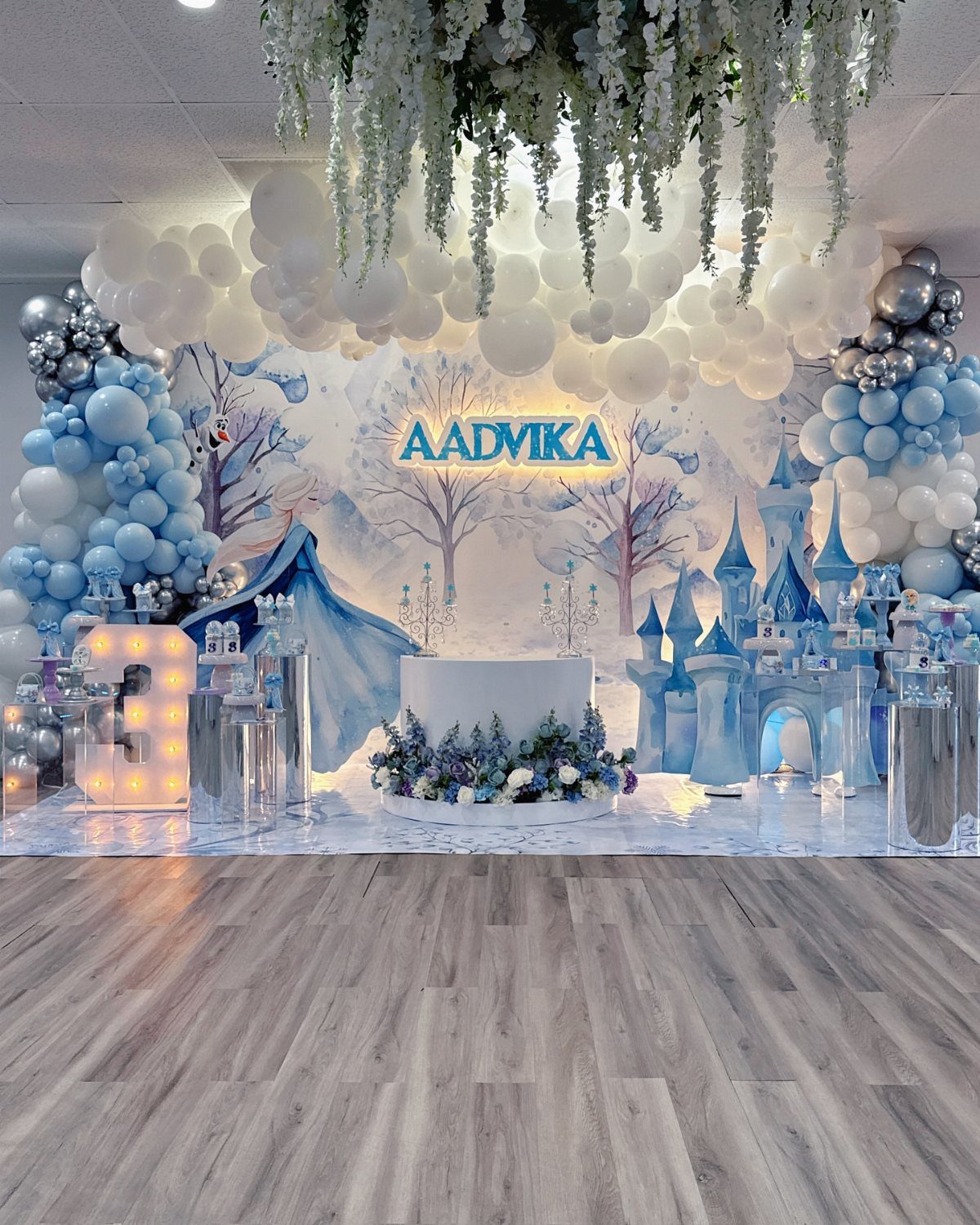 Winter wonderland party setup with blue balloons, snowy backdrop, and a blue castle.