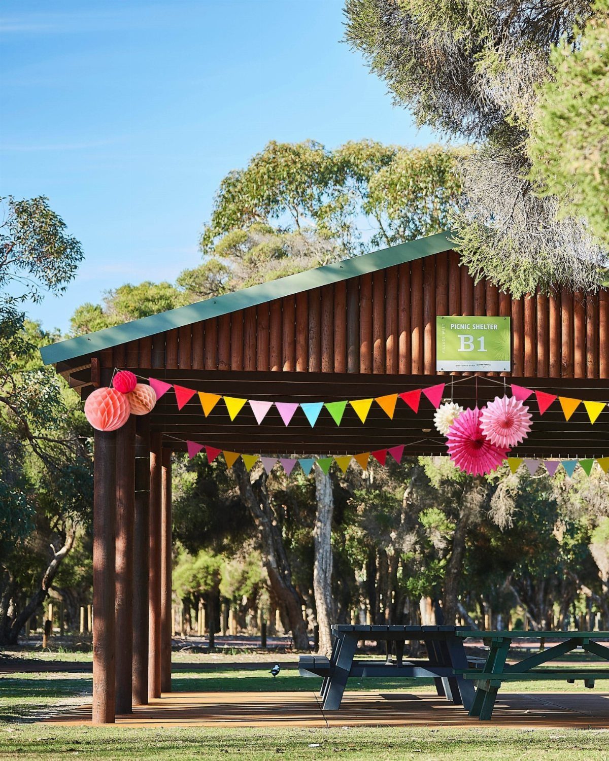 Wooden park pavilion decorated with colorful bunting and pink pom-poms for a party.
