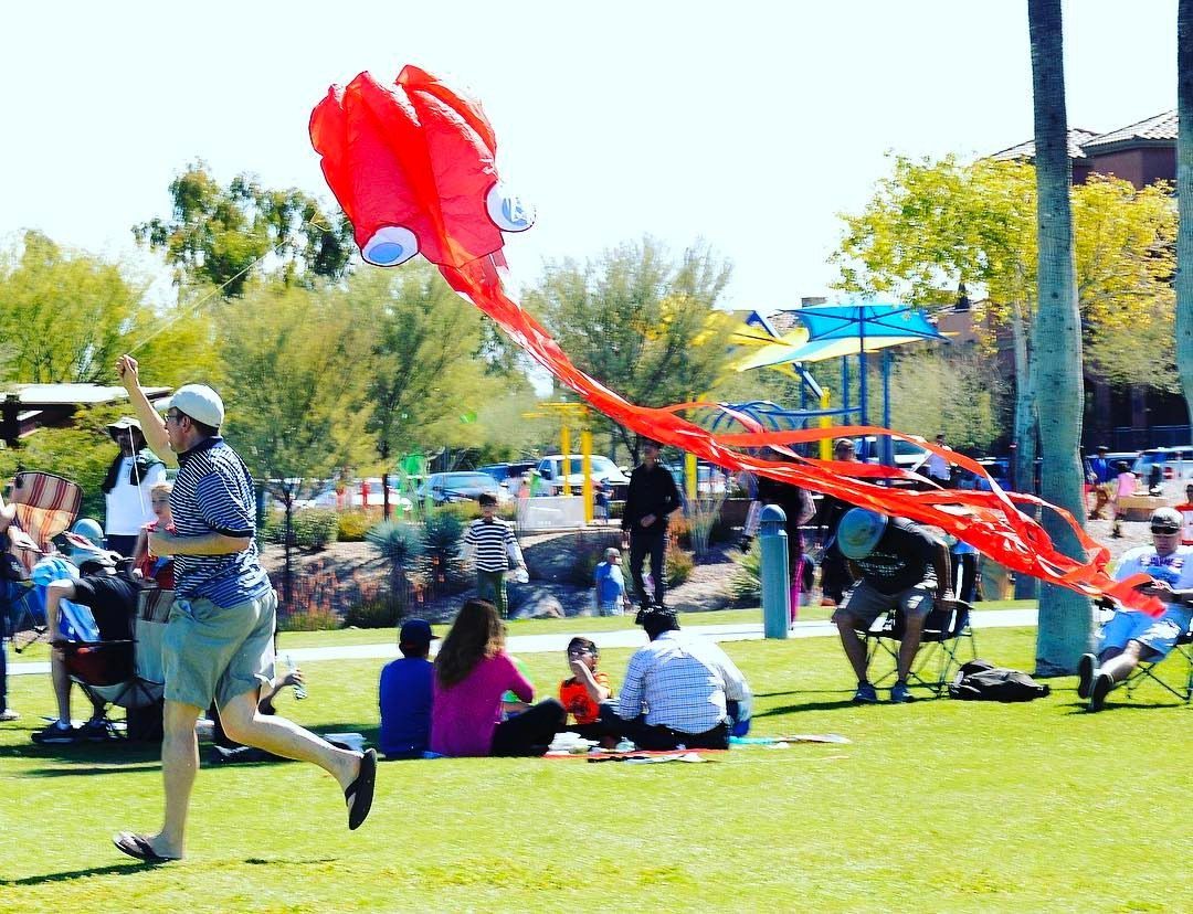 Man flying a large red octopus kite in a sunny public park.
