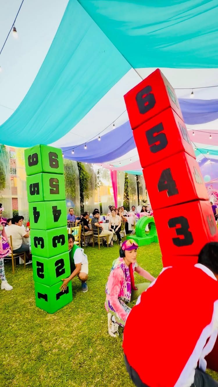 Children playing with giant numbered foam blocks on a lawn under a colorful canopy.