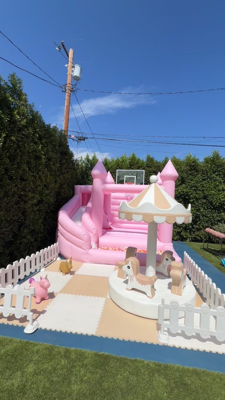 Pink inflatable bounce house with slide and white picket fence on a lawn
