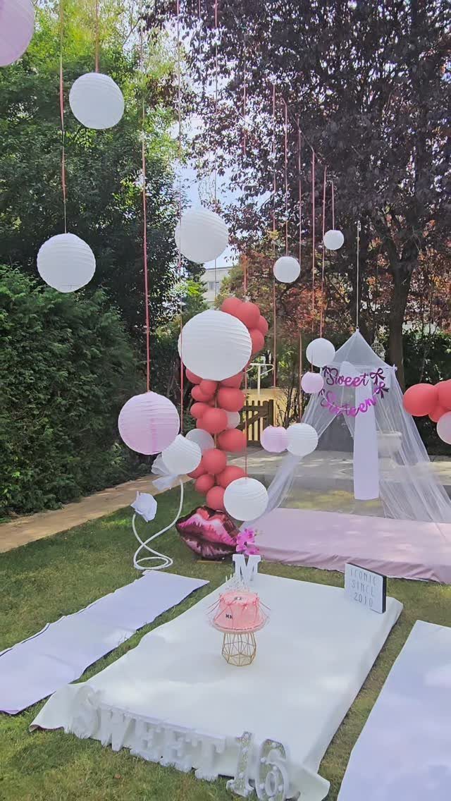 Outdoor birthday party setup with pink balloons, white lanterns, and a picnic teepee.