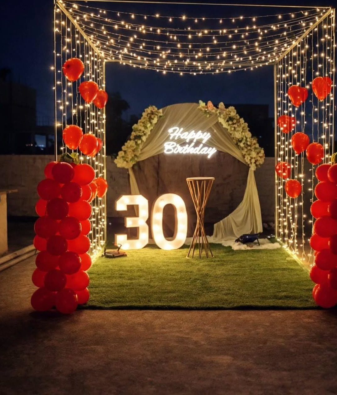 Nighttime birthday party setup with string lights, red balloons, and glowing number 30.