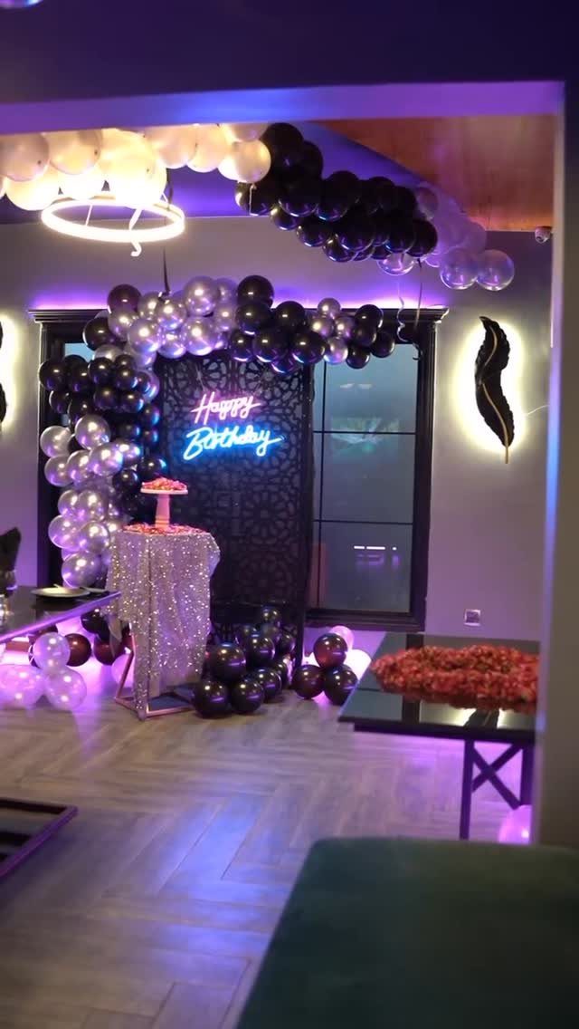 Birthday party room decorated with black and silver balloons and neon sign.