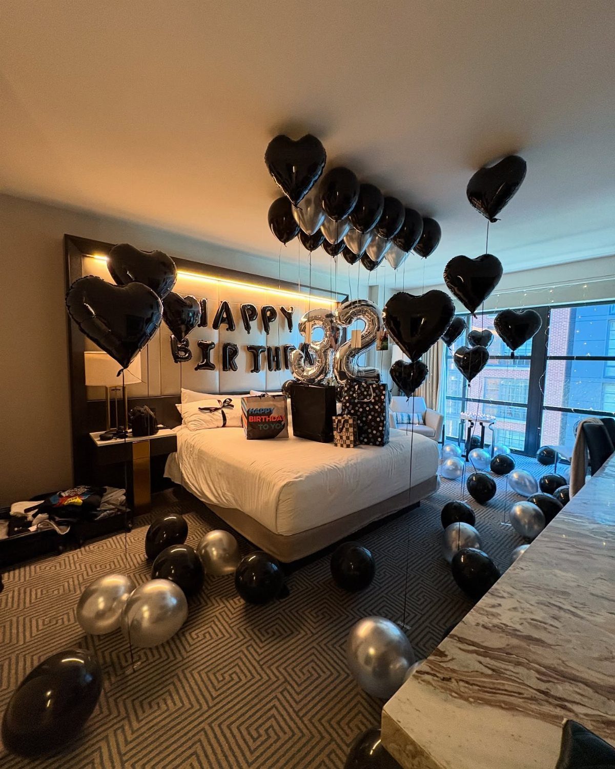 Hotel bedroom decorated with black and silver heart balloons for a 32nd birthday.