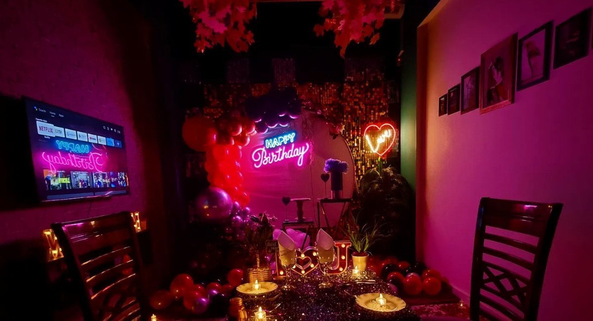 Birthday party room with red neon signs, balloons, and a candlelit dinner table.