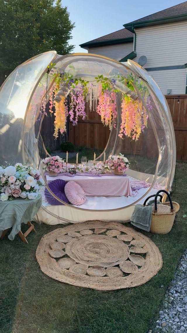 Clear bubble tent party setup with pink flowers, low table, and purple cushions