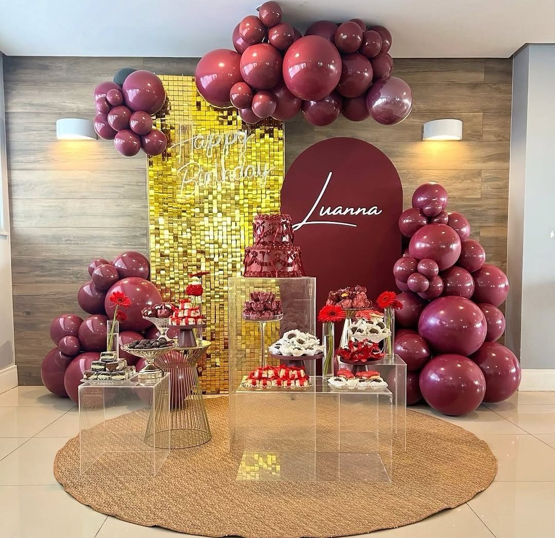 Burgundy and gold birthday party decoration with balloons, cake, and dessert table.