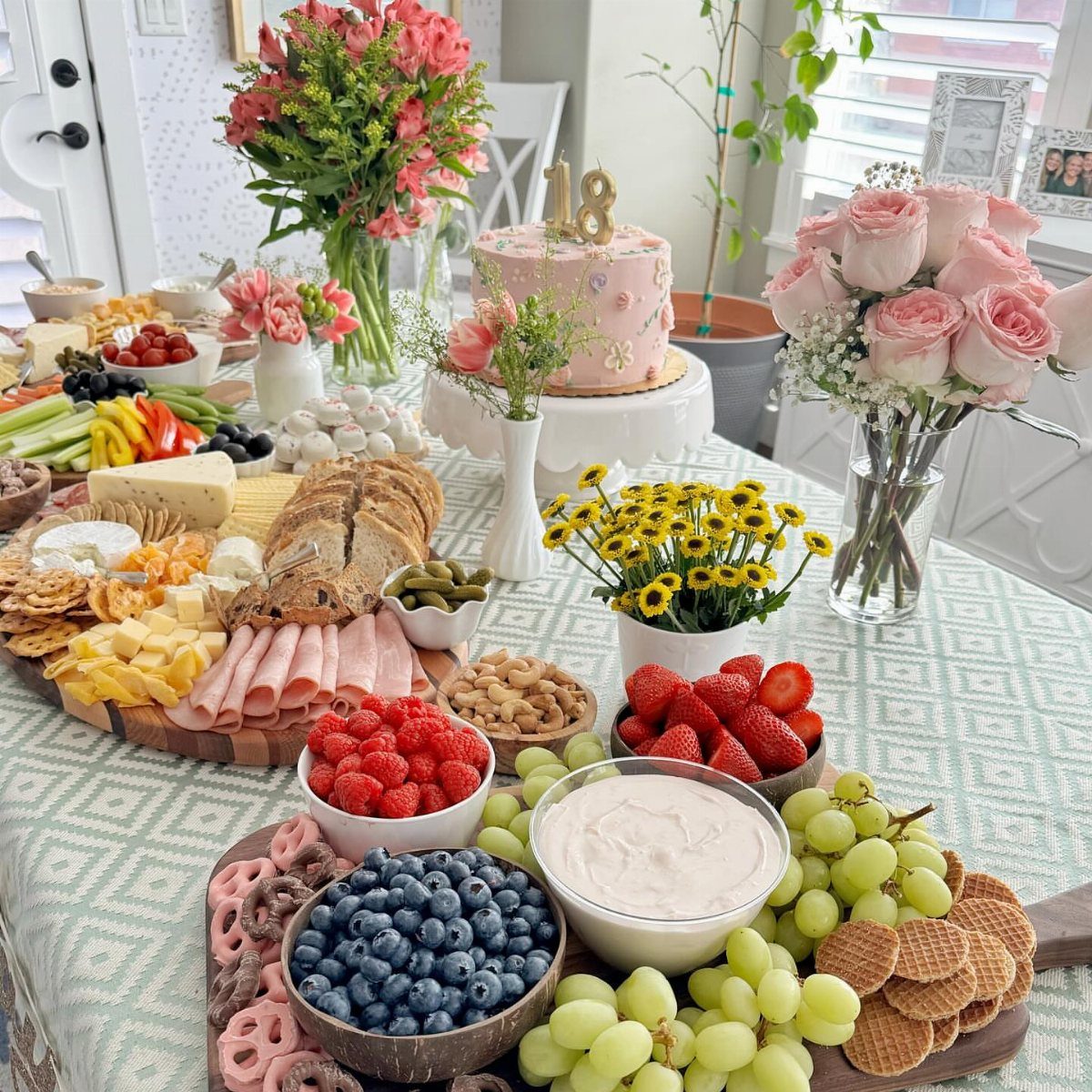 Charcuterie board with fruits, cheeses, and meats next to an 18th birthday cake.