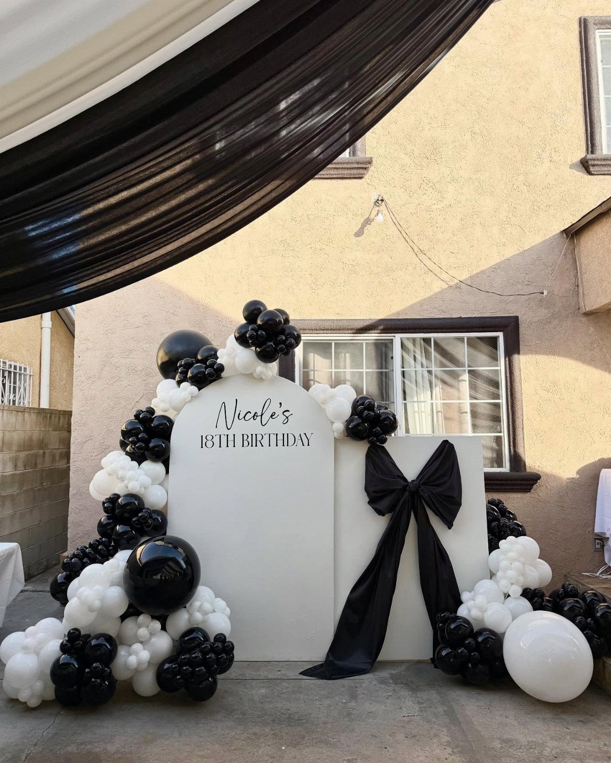 Black and white 18th birthday backdrop with balloons and a large black bow.