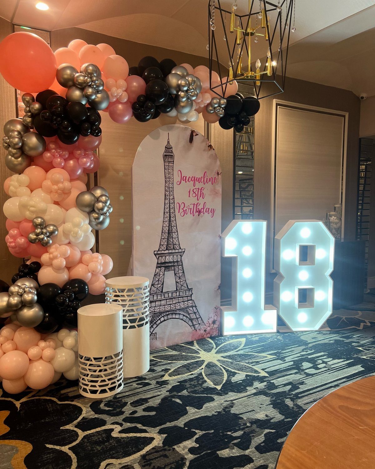 Birthday party decoration with pink and black balloons, Eiffel Tower backdrop, and glowing 18 numbers.